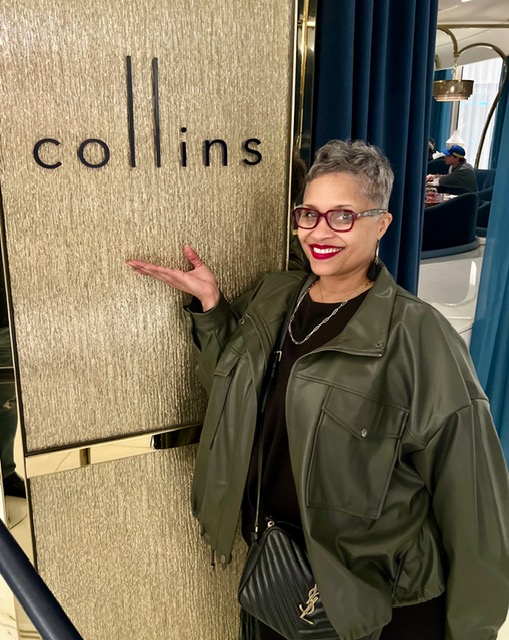 Chef Malika smiling beside a Collins sign